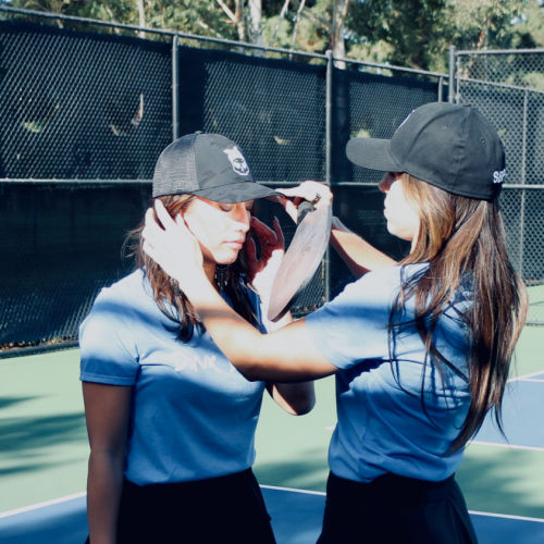 Two girls putting on Black Skull Caps from Soul Bandit Pickleball at the court